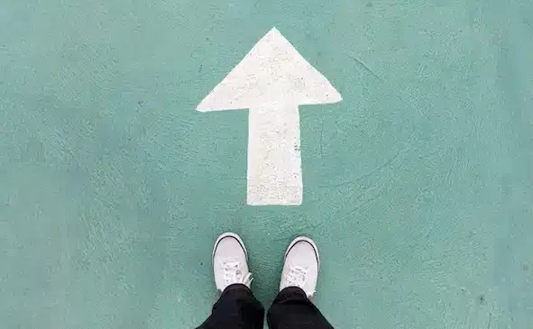 Auf dem Betonboden stehende Schuhe und weißes Wegweiser, um weiter zu gehen