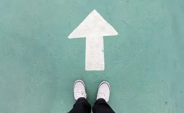 Auf dem Betonboden stehende Schuhe und weißes Wegweiser, um weiter zu gehen