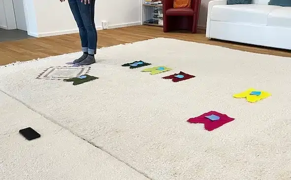 Eine Aufstellung mit Filzchen als Stellvertreter. Man sieht die Füsse einer Person und sieben Filzchen.